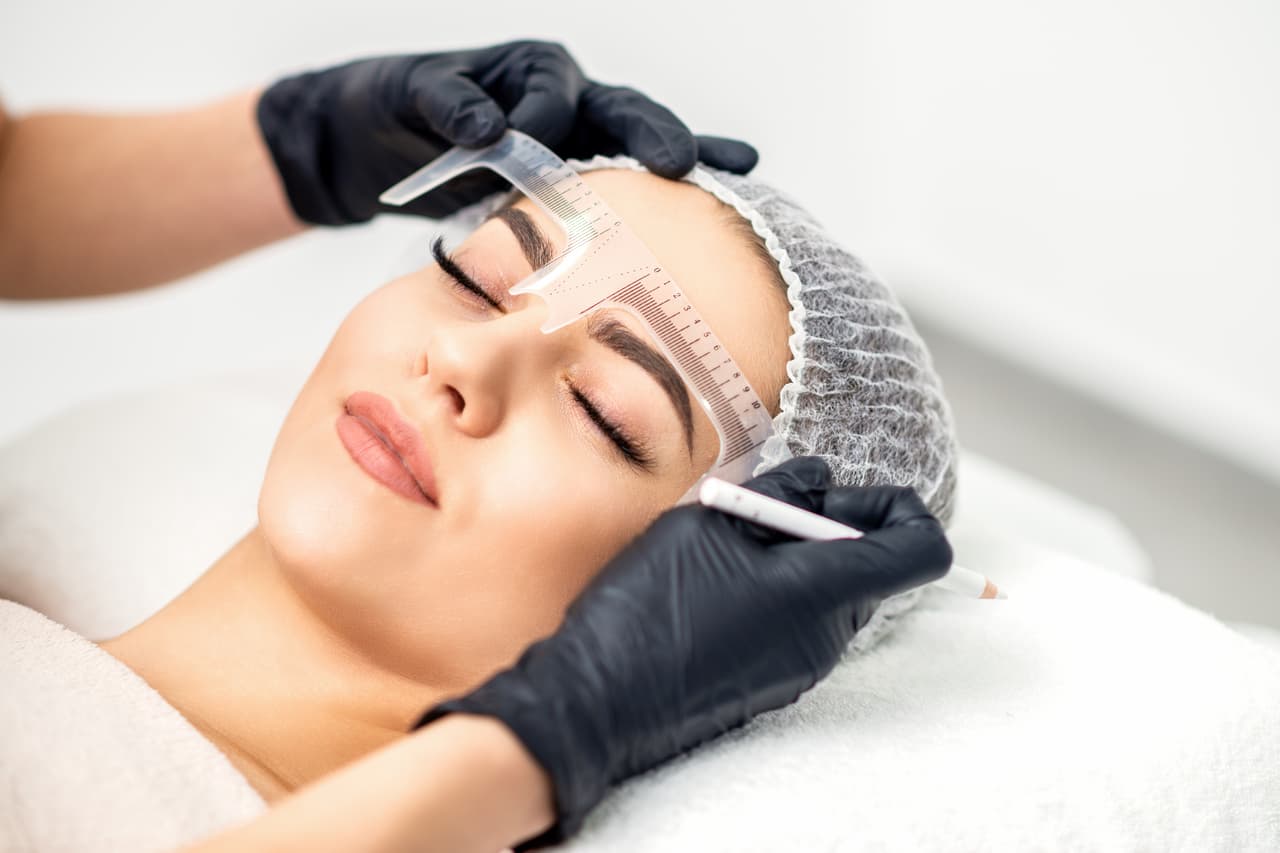 Beautician is measuring the brows with ruler before tattooing eyebrows