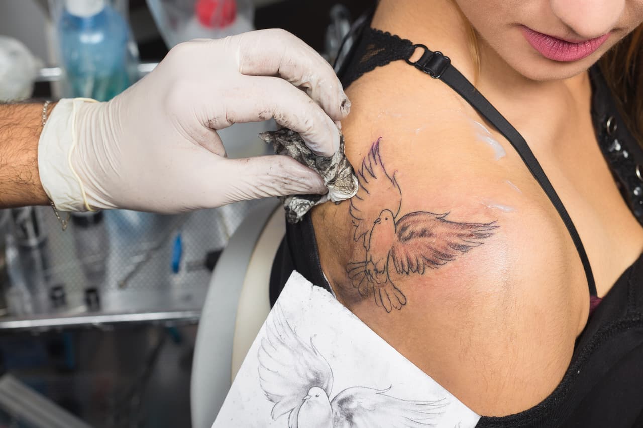 Tattoo master tattooing on the a girl back. In the tattoo salon.