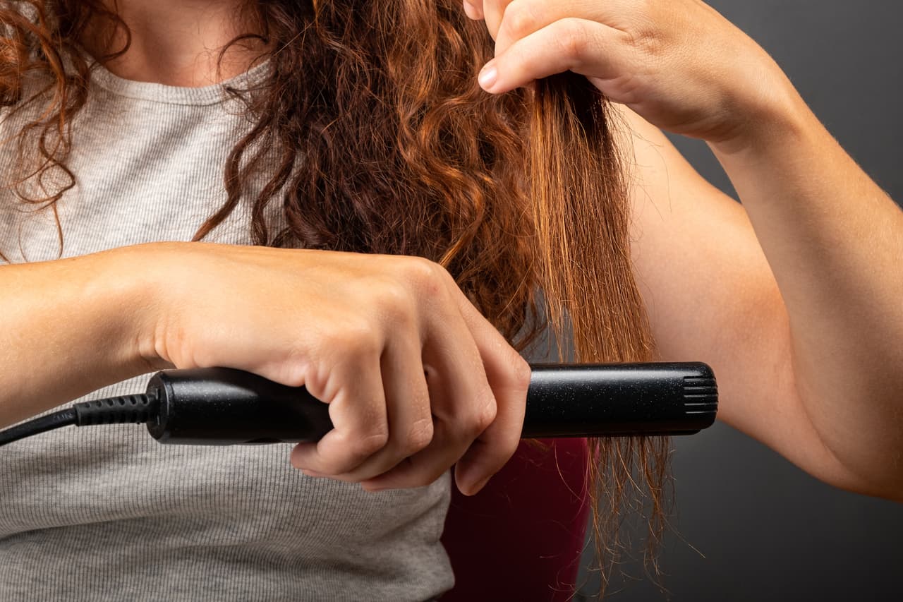 girl smooths curly hair with a hair straightener, curling iron.