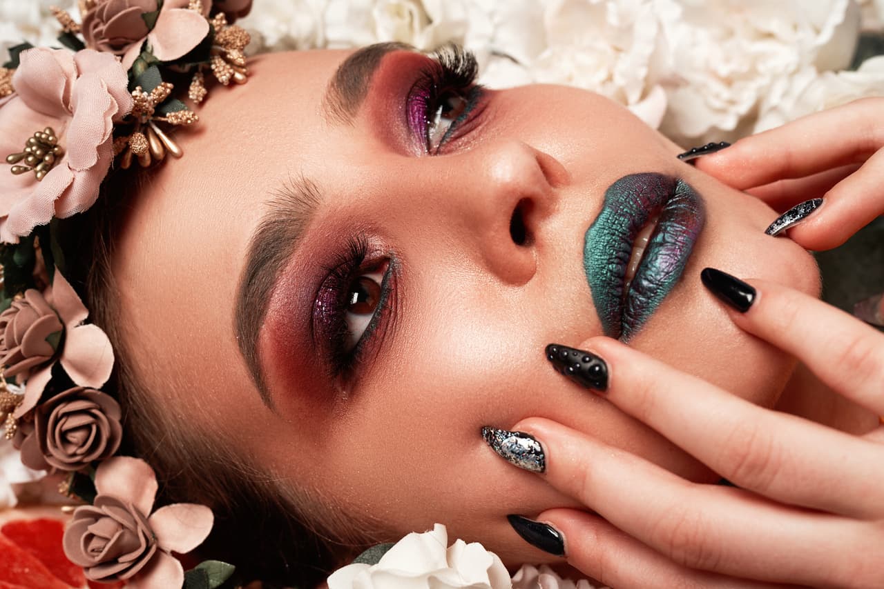 Beautiful brunette fashion model with strange makeup posing on flowerbed surrounded by plants and fruit, looking away
