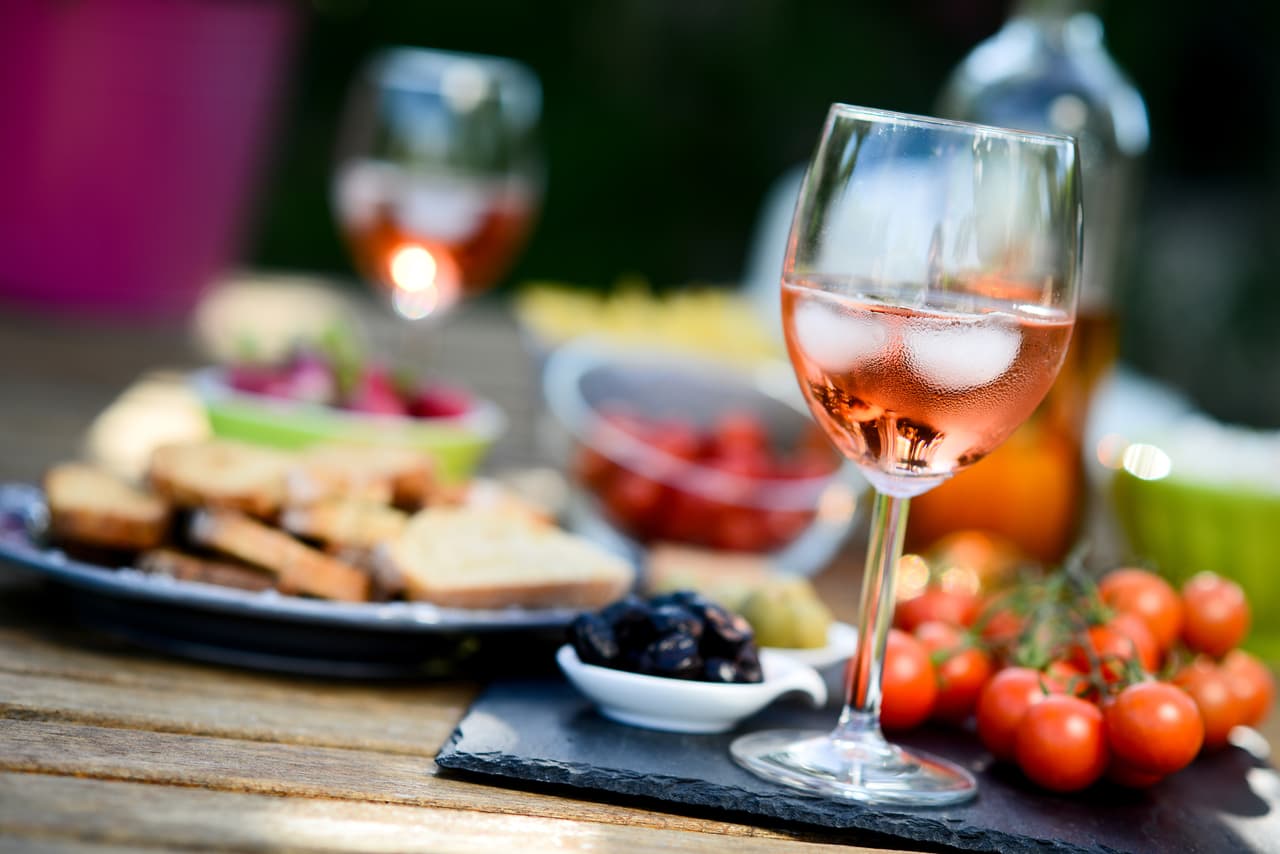 holiday summer brunch party table outdoor in a house backyard with appetizer, glass of rosÃ© wine, fresh drink and organic vegetables