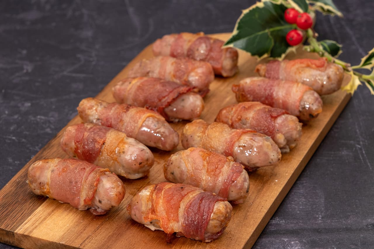 Pigs in blankets or sausages wrapped in bacon on a wooden board