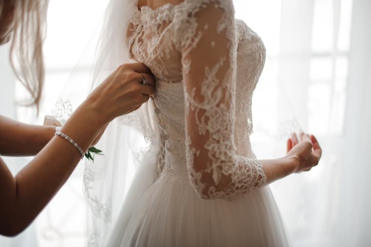 Bridesmaid making a bow-knot on the back of brides lacy white and beautiful wedding dress