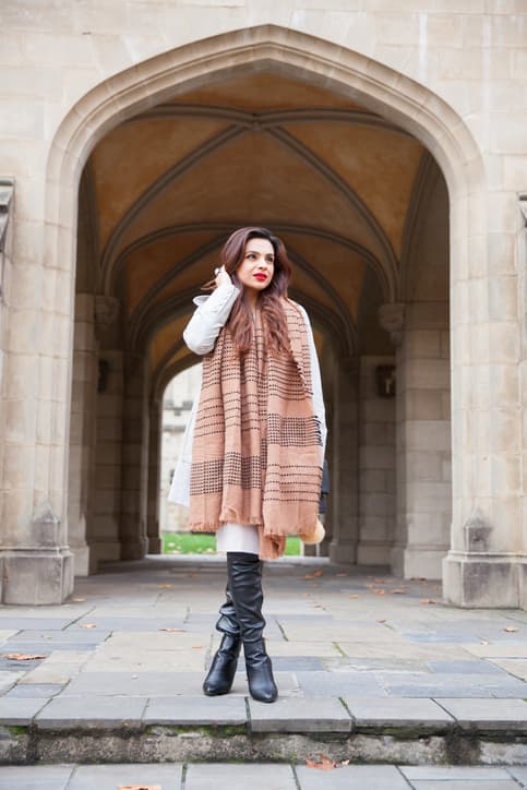 A fashionable dressed young woman standing in front of a beautiful arch. She is standing and waiting, with hand in her hair.
