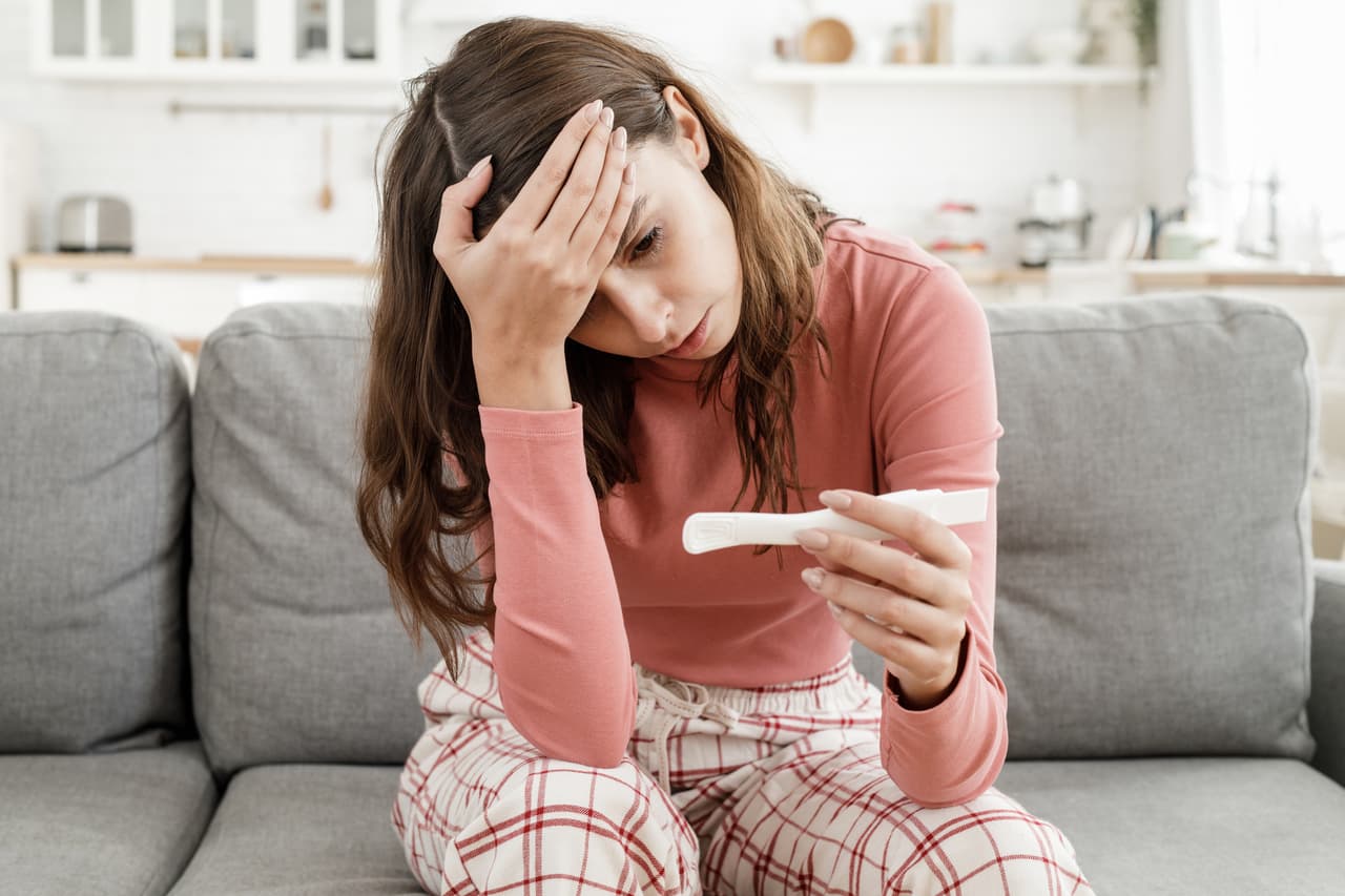 Young European woman worried because she has got positive results of pregnancy test, sitting alone at home