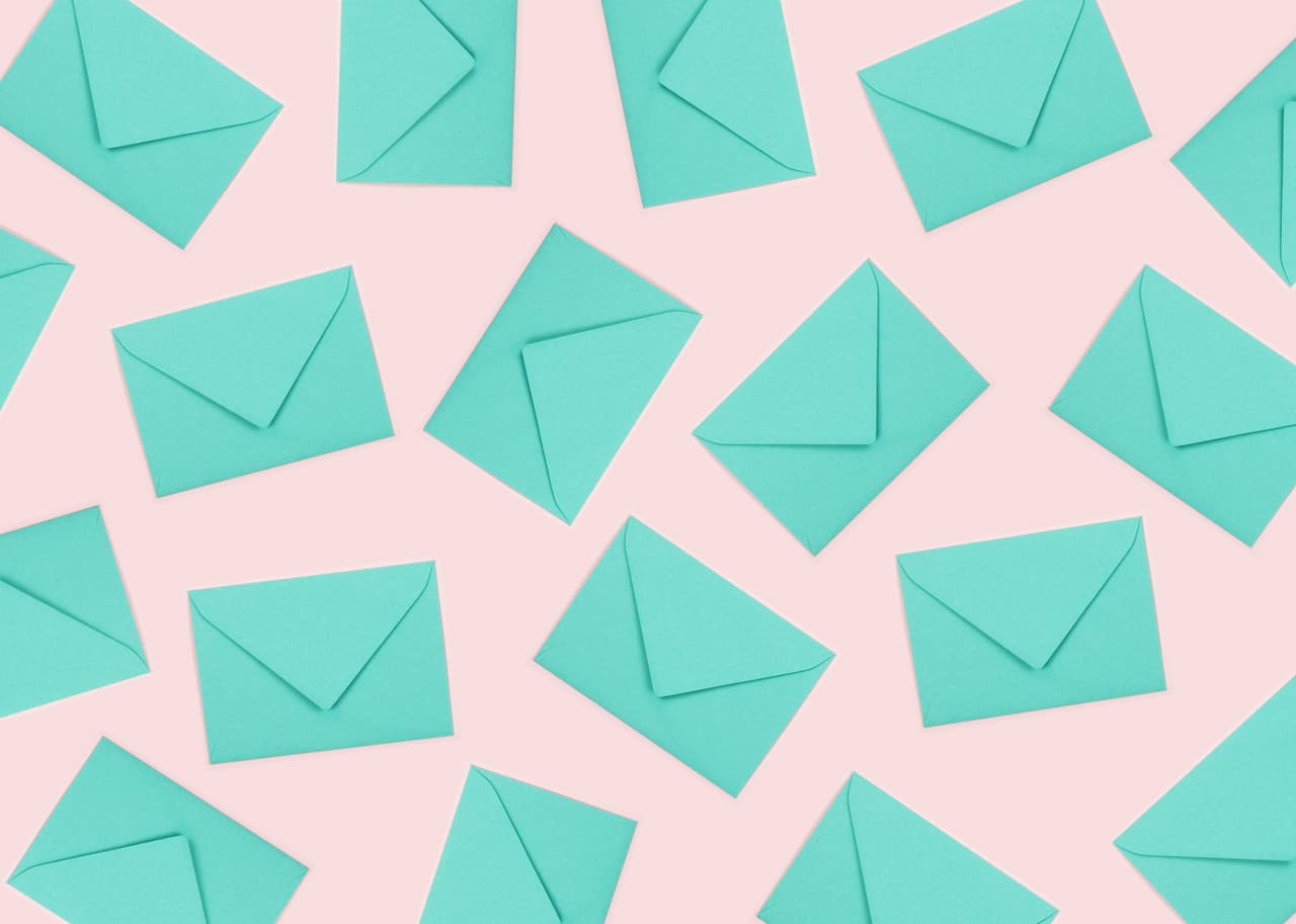 Creative pattern made of bright turquoise envelopes on pastel pink background.