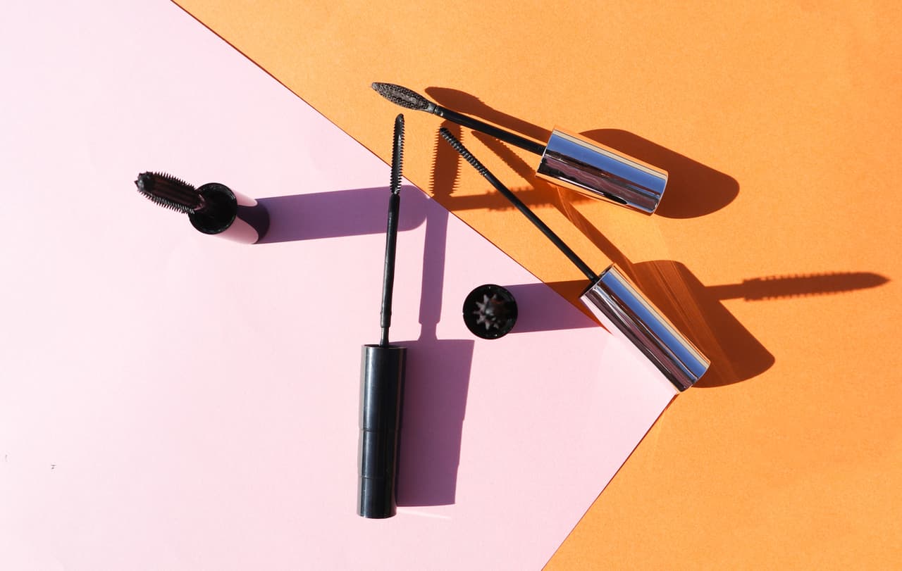 makeup brush nail polish eyelashes skin care products flat lay on a pastel background