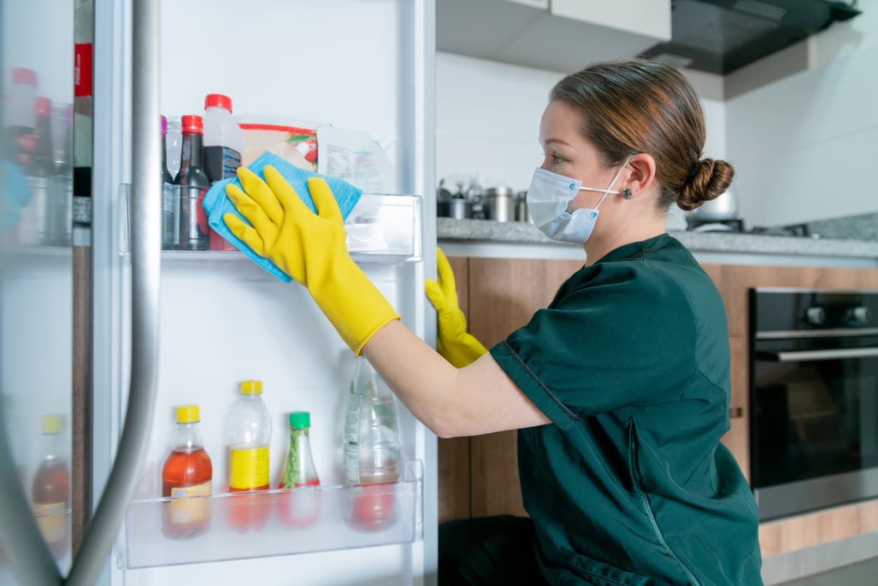 Latin American cleaner wearing a facemask while cleaning the fridge during the COVID-19 pandemic