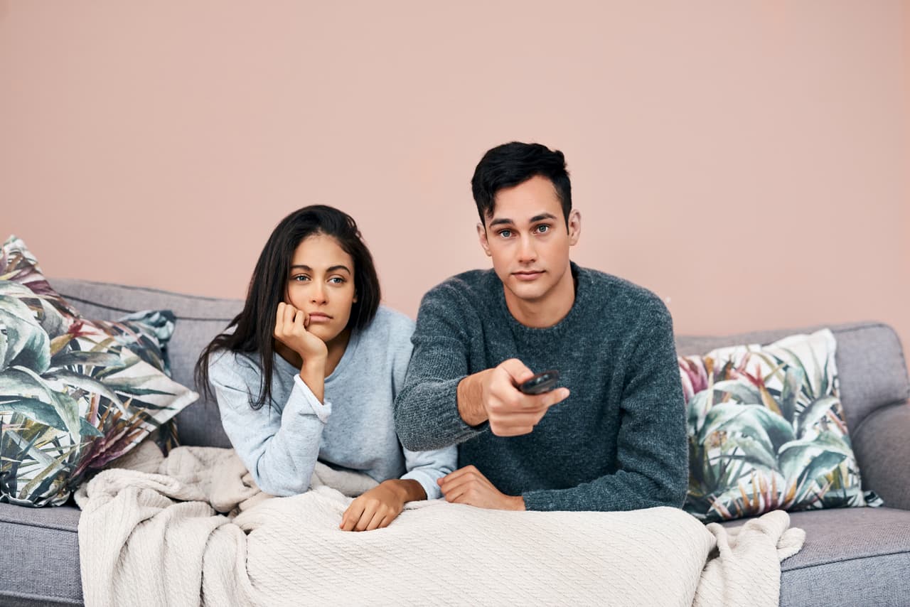 Shot of a young couple watching tv while recovering from an illness at home