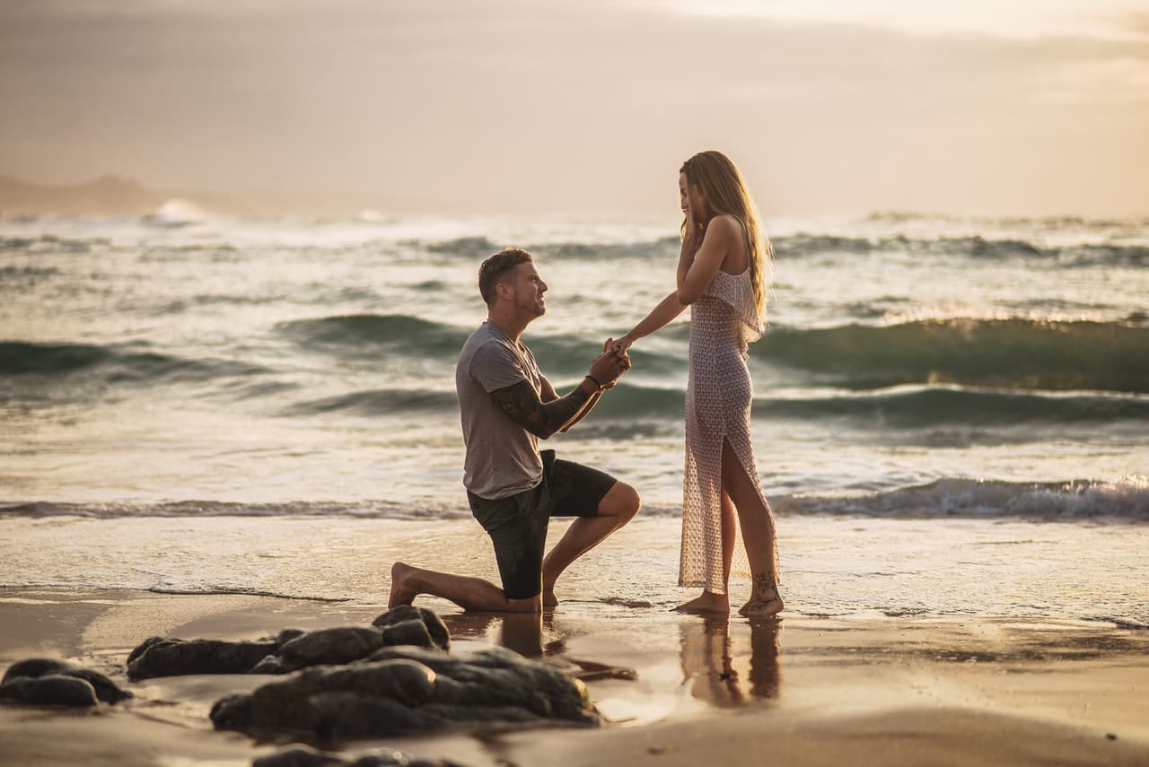 Young man kneeeling, proposing to his girlfriend by the sea
