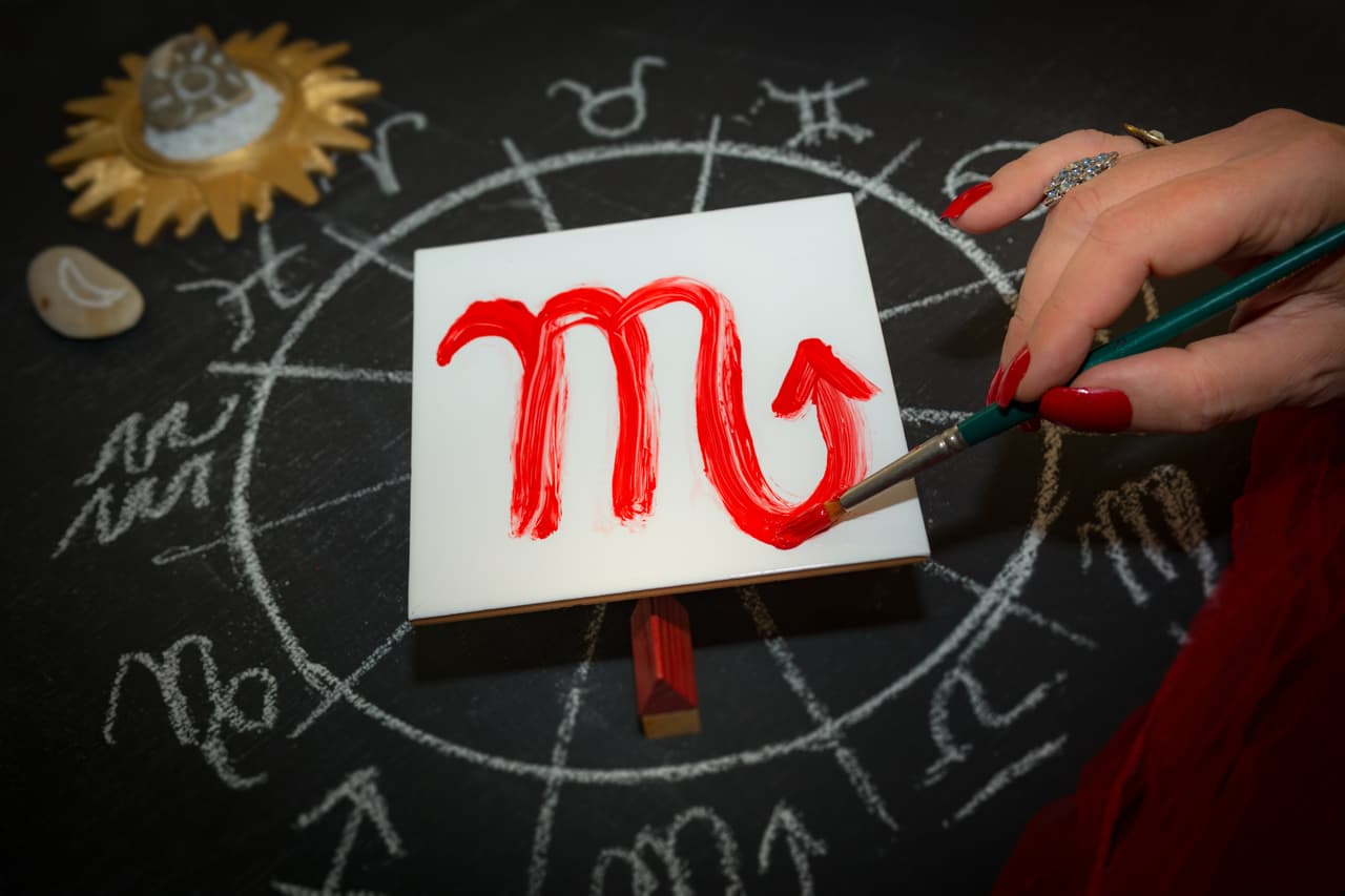 Mature woman astrologer with red nails draws a zodiac sign on a white tile above the full zodiac drawn on a blackboard with white chalk in a circle. All drawings made by contributor. Western astrology is based on the construction of a horoscope for an exact moment, such as a person's birth. It uses the tropical zodiac, which is aligned to the equinoctial points.