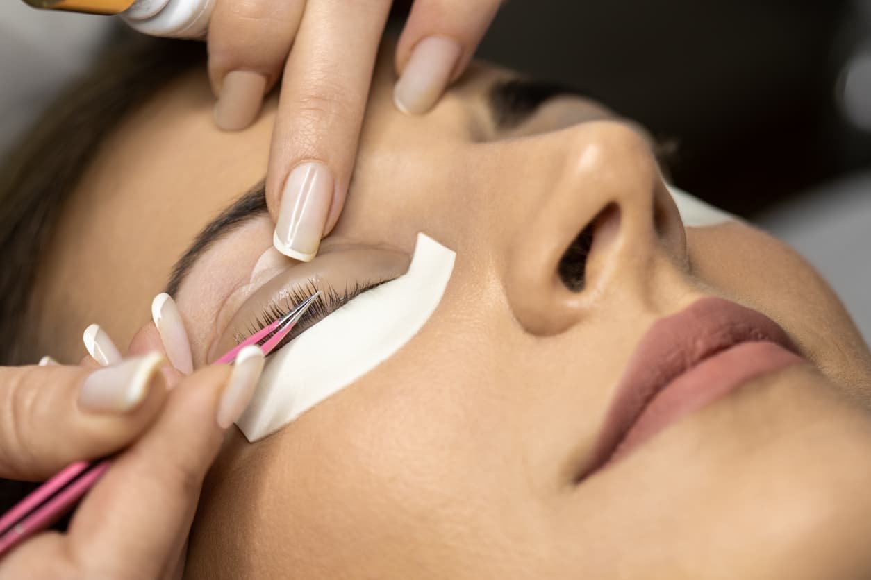 Beautiful young woman with beautiful clean skin having a lash lift treatment. She is laying on the bed, her eyes are closed and the beautician is doing the treatment.