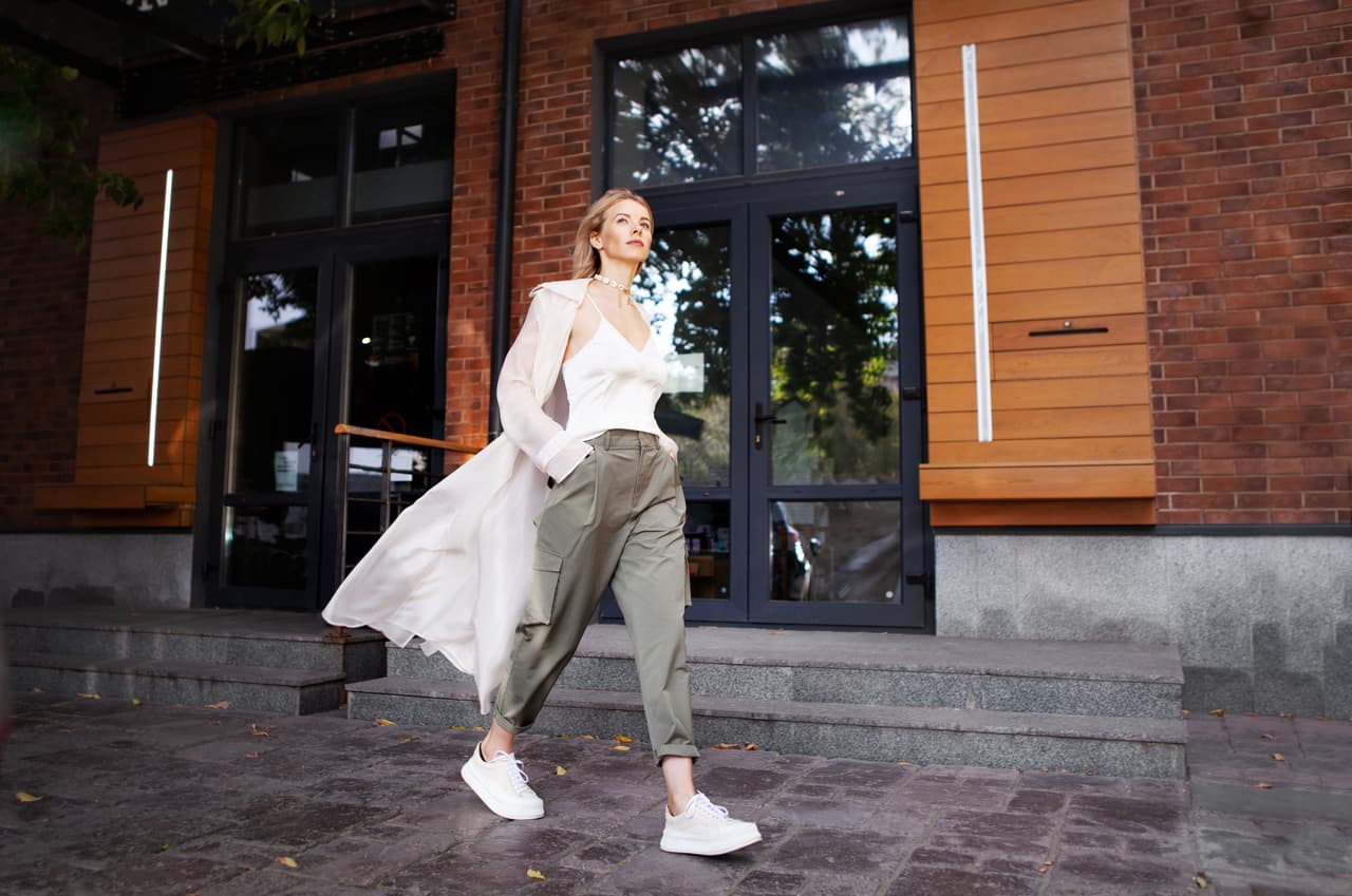 Beautiful Sexy Woman Wearing Fashionable Spring or Fall Clothes (beige trench coat, oversize khaki cargo pants, accessorie) Outdoors. Female stylish Model walking city Street. Autumn trend, street fashion outfit