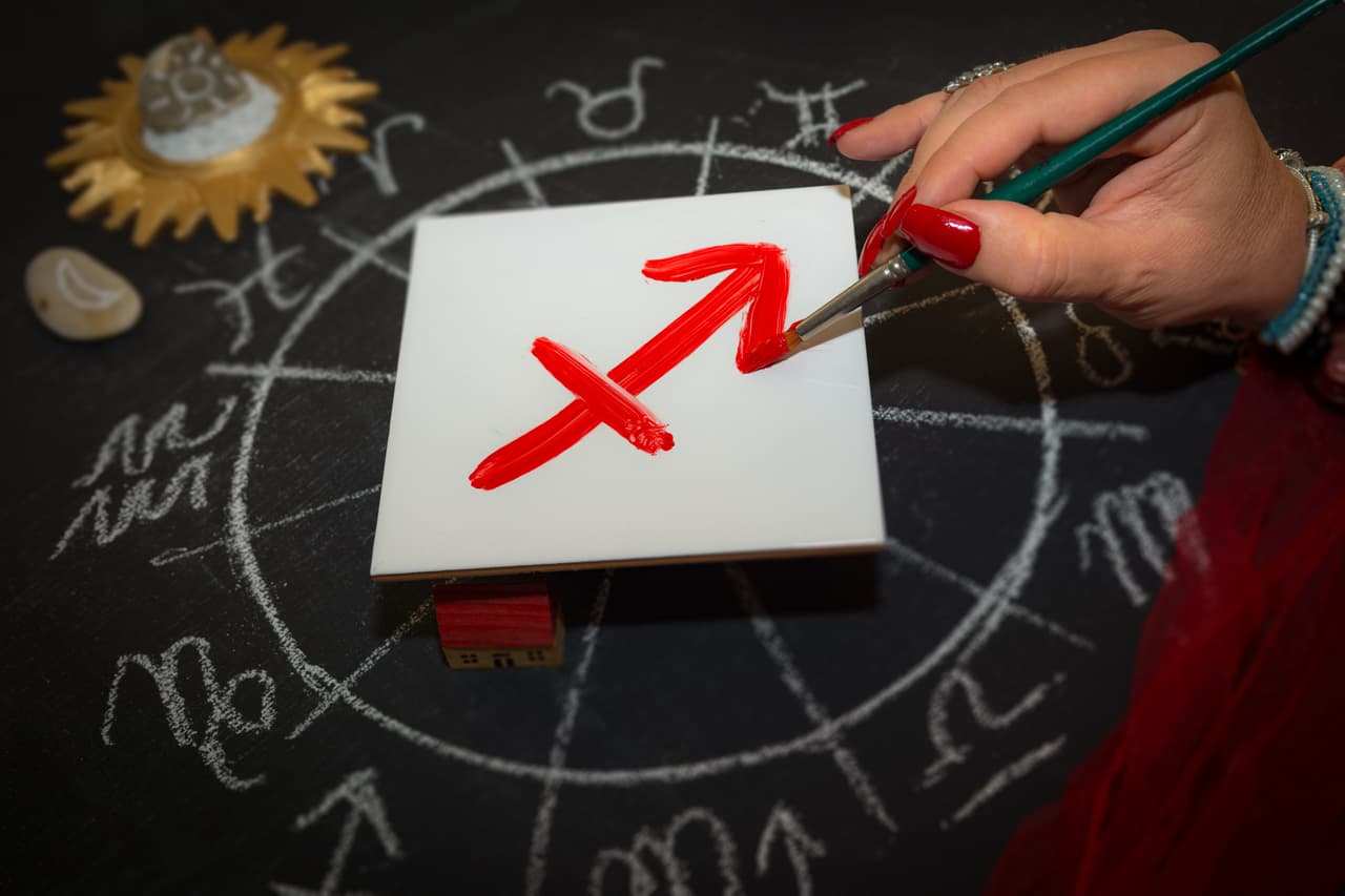 Mature woman astrologer with red nails draws a zodiac sign on a white tile above the full zodiac drawn on a blackboard with white chalk in a circle. All drawings made by contributor. Western astrology is based on the construction of a horoscope for an exact moment, such as a person's birth. It uses the tropical zodiac, which is aligned to the equinoctial points.