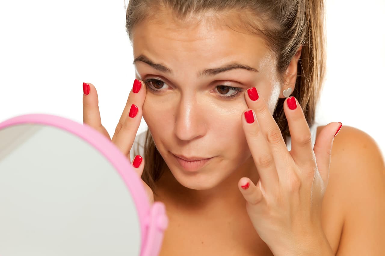 young women applied concealer under the eyes with her fingers