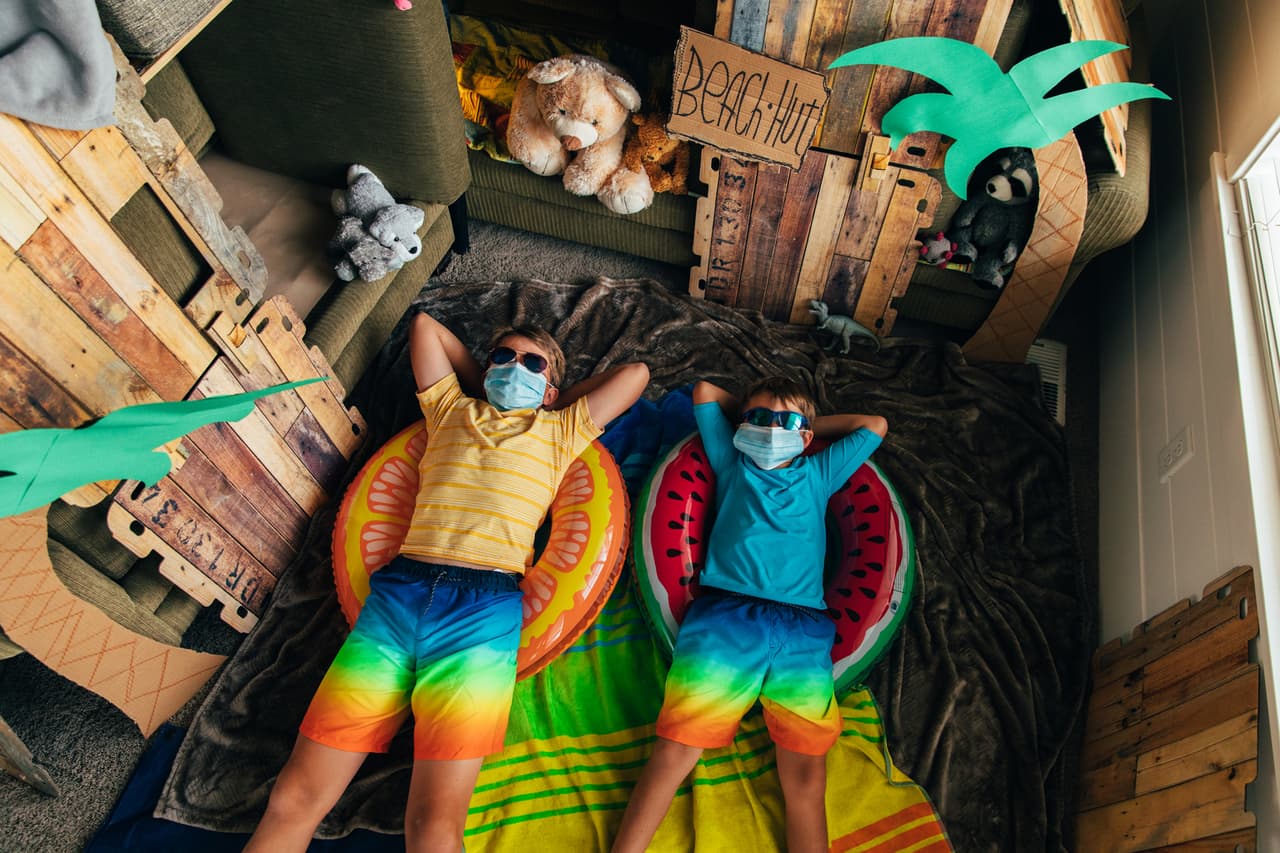 Young brothers are ready to go to the beach they have made in their home. The coronavirus quarantine has forced them from vacation mode to staycation mode. They are using the imagination by building couch fort into a beach hut.