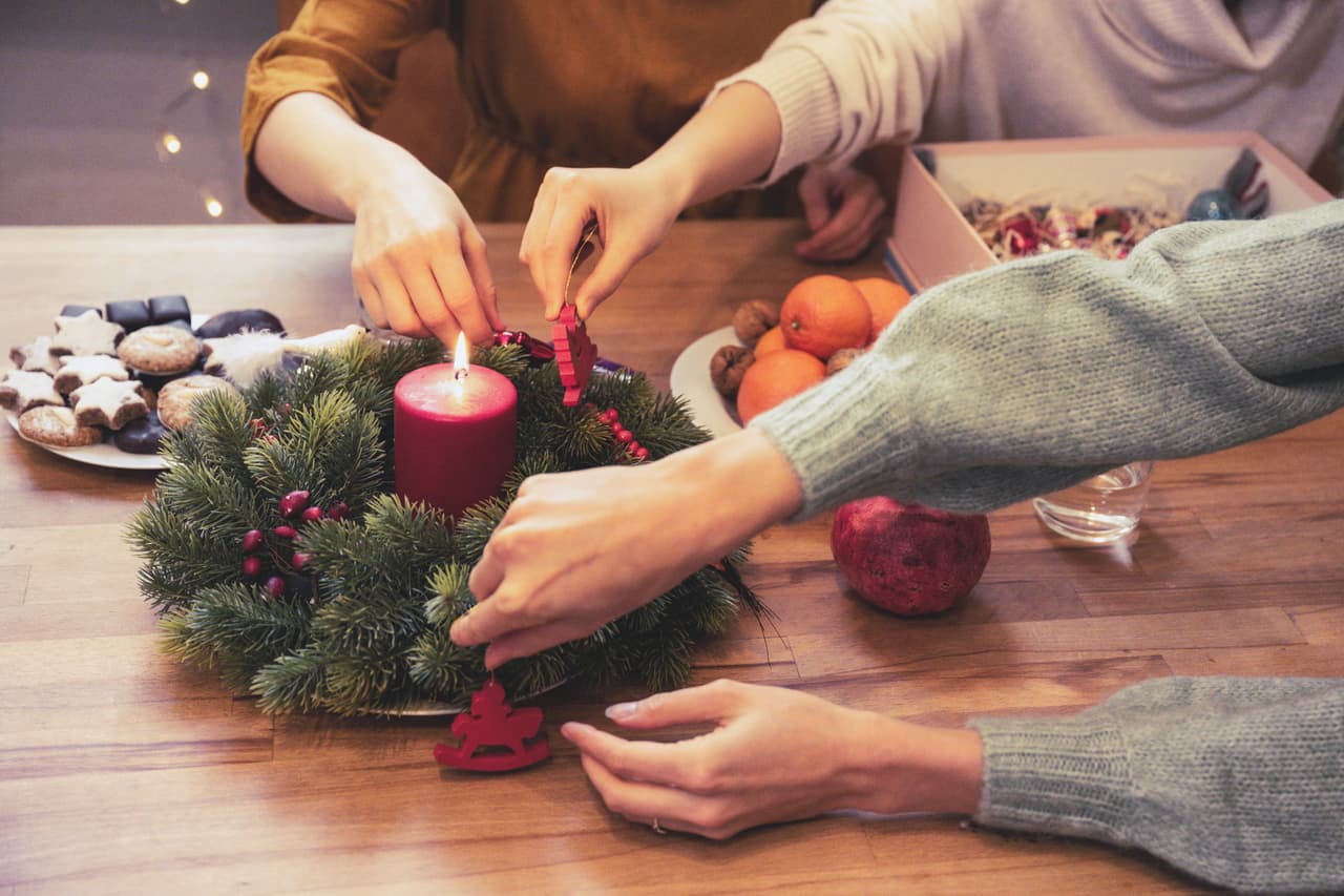 close up of three young womans hands decorating together advent wreath on wooden table in the kitchen