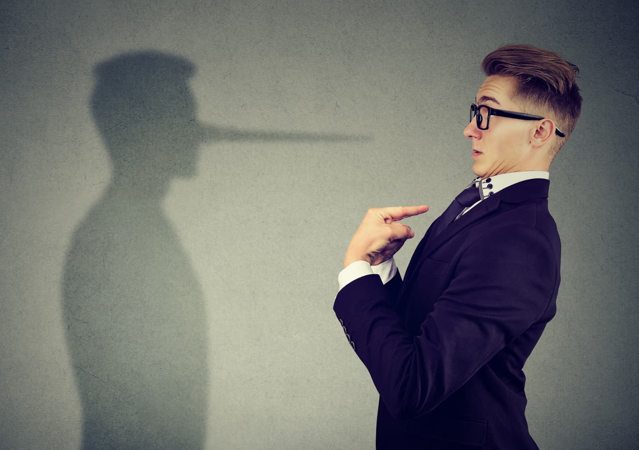 Side view of man in suit pointing at himself looking at shadow with long nose of a liar.