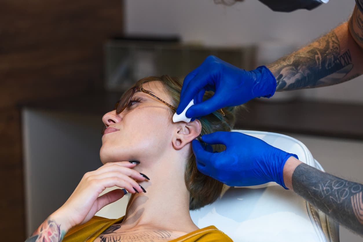Portrait of woman getting her ear pierced. Man showing a process of piercing ear. Cleaning the ear and making it sterile. Ear Piercing Procedure. Body Piercing. Beautiful woman getting her ear pierced