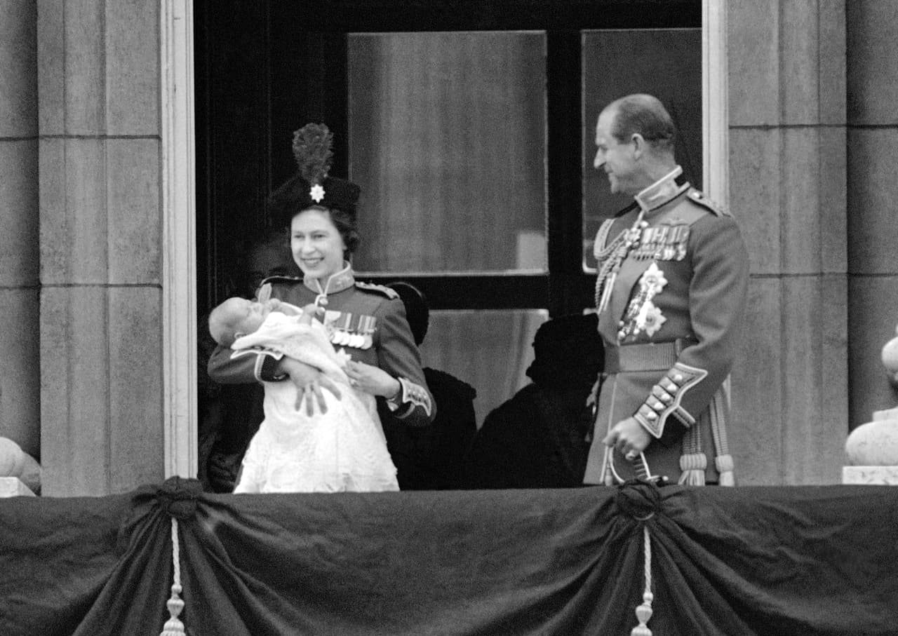 Para 1964, vestida en una túnica color escarlata, la reina Isabel II cargo al príncipe Edward, el cuarto y último de sus hijos, mientras saludaba al público en las afueras del palacio de Buckingham.