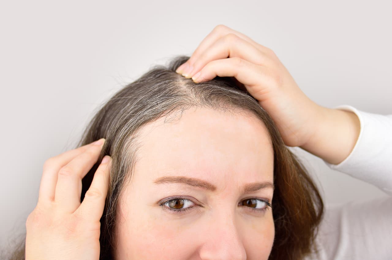 woman is checking white hair while looking at the mirror