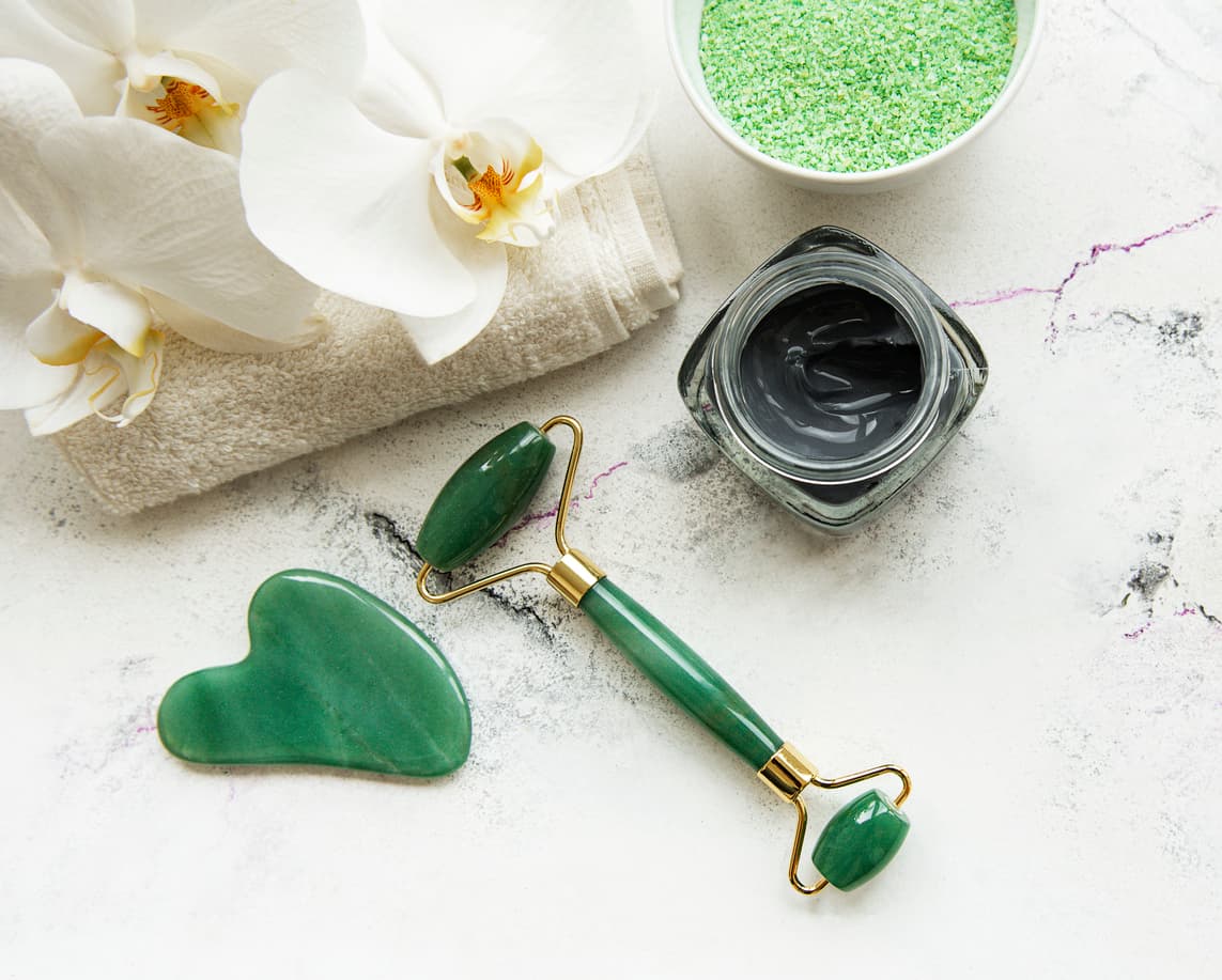 Skincare morning beauty routine at home bathroom - face jade roller massager for wellness cosmetic therapy, mask and orchid flowers on marble background
