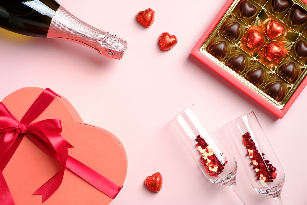Happy Valentines Day concept. Flat lay, top view box of chocolates, champagne glasses with confetti, heart-shaped box, champagne bottle