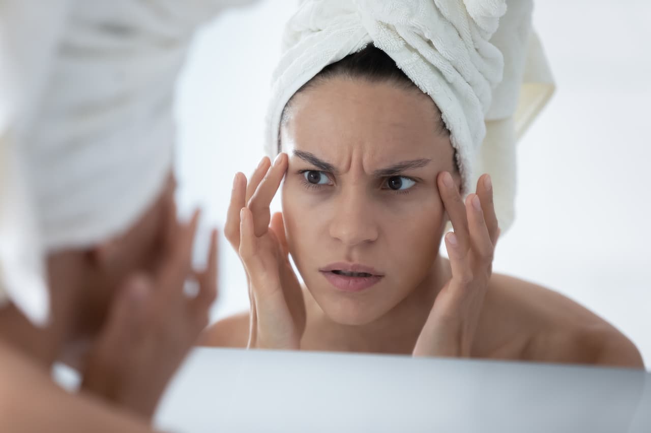 Close up unhappy woman wearing white bath towel checking skin after shower, looking in mirror, worried about mimic wrinkle or acne, touching face skin, facial cosmetology, treatment, skincare concept