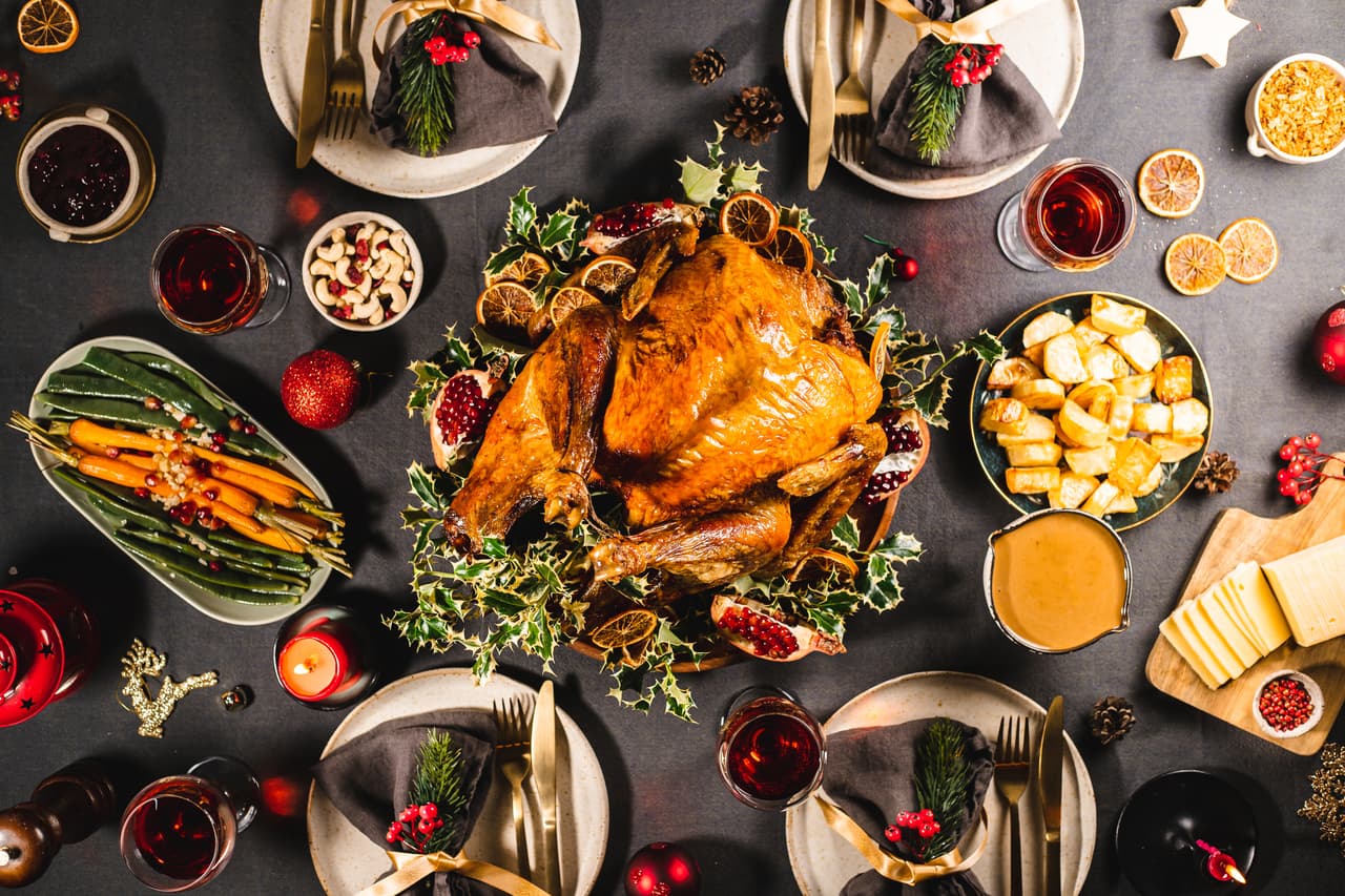 Directly above view of a delicious Christmas meal with roasted Turkey, carrots, cashews, pomegranates, dried oranges and red wine on the dinner table.