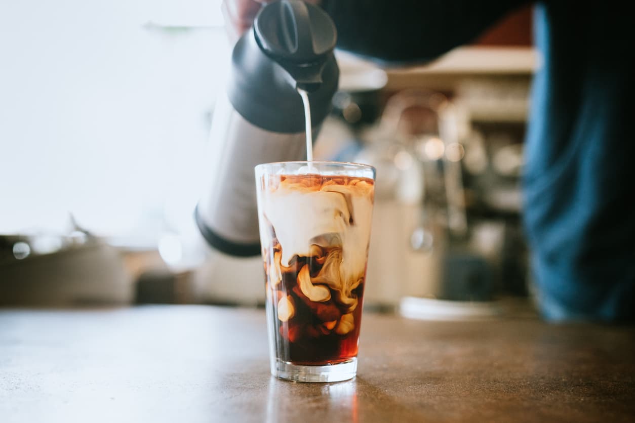A man pours cold whole milk in to a glass of iced coffee in a cafe. A cool refreshing drink for a hot summer day.