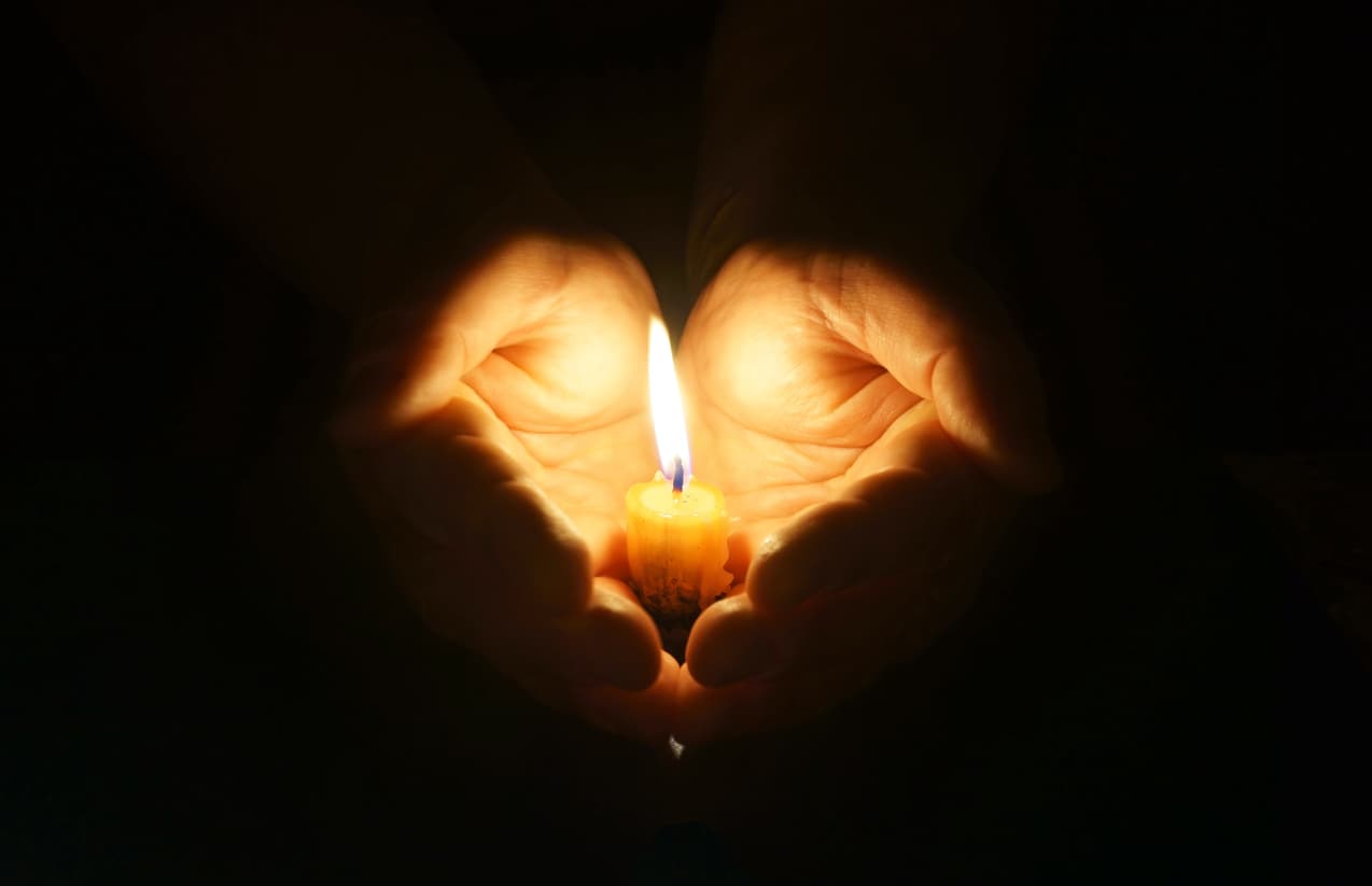 Man hands holding a burning candle in dark. Cupped hands with burning candle. Gentle protection of fragile fire.